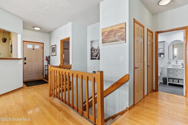 corridor with a sink, a textured ceiling, wood finished floors, and an upstairs landing
