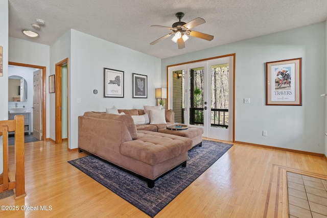 living area featuring a ceiling fan, baseboards, light wood-style flooring, and a textured ceiling