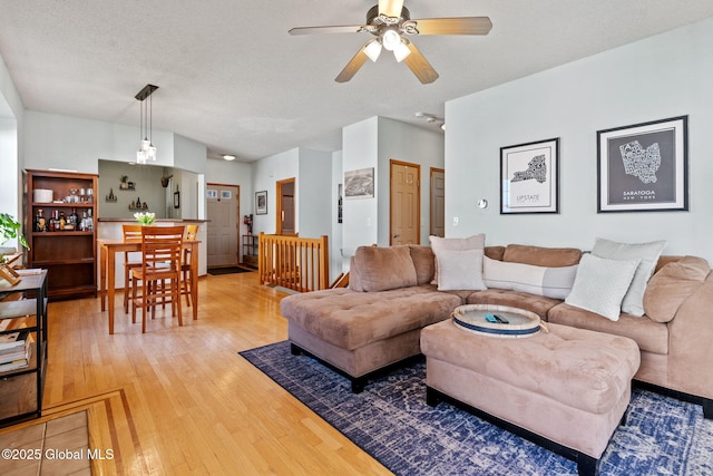 living room with a ceiling fan, light wood finished floors, and a textured ceiling