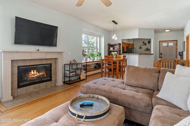 living room with a textured ceiling, ceiling fan, wood finished floors, and a tile fireplace
