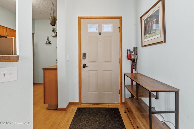 foyer featuring a textured ceiling, baseboards, and light wood-style flooring