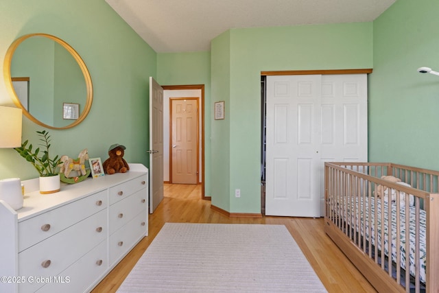 bedroom featuring a nursery area, a closet, and light wood finished floors