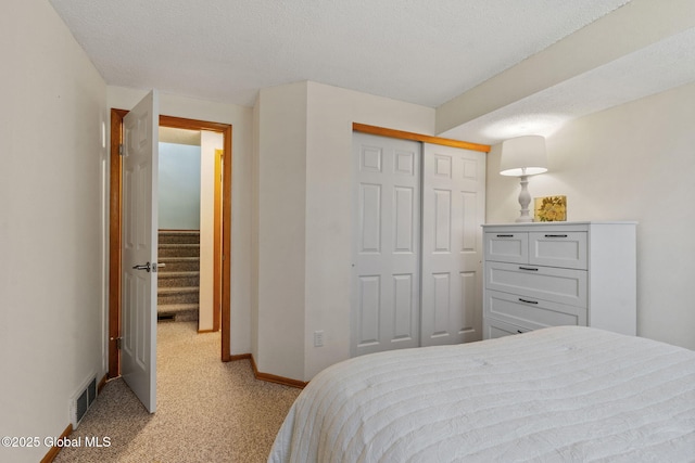 bedroom with light carpet, a textured ceiling, baseboards, visible vents, and a closet