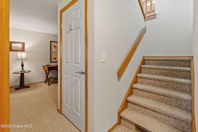 staircase featuring carpet floors, a textured ceiling, and baseboards