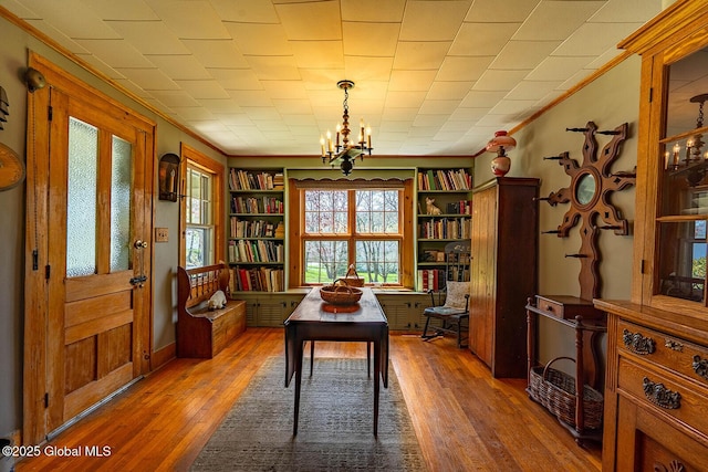 office area featuring wood-type flooring, crown molding, a notable chandelier, and built in features
