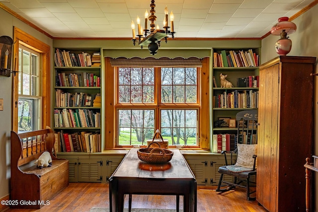 living area featuring built in features, ornamental molding, wood finished floors, and a notable chandelier