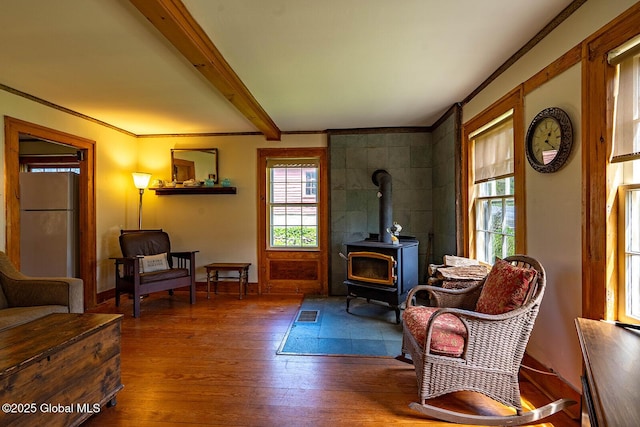 living area with crown molding, a wood stove, beam ceiling, wood finished floors, and baseboards