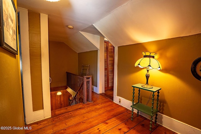 interior space featuring wood-type flooring, baseboards, an upstairs landing, and vaulted ceiling