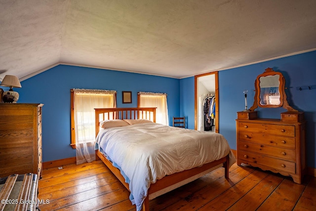 bedroom featuring a closet, baseboards, a spacious closet, hardwood / wood-style flooring, and vaulted ceiling