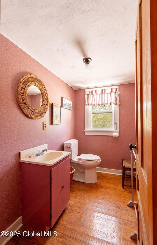 half bathroom featuring wood-type flooring, toilet, baseboards, and vanity