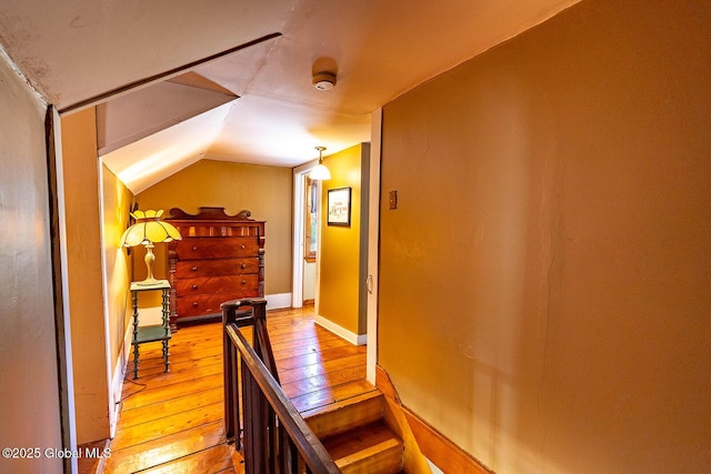 hall with light wood-style floors, lofted ceiling, and an upstairs landing