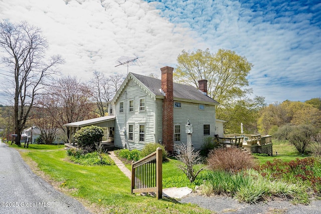 view of side of home with a wooden deck, a yard, and a chimney