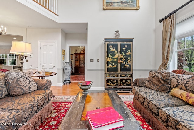 living area featuring a towering ceiling, wood finished floors, baseboards, and a chandelier