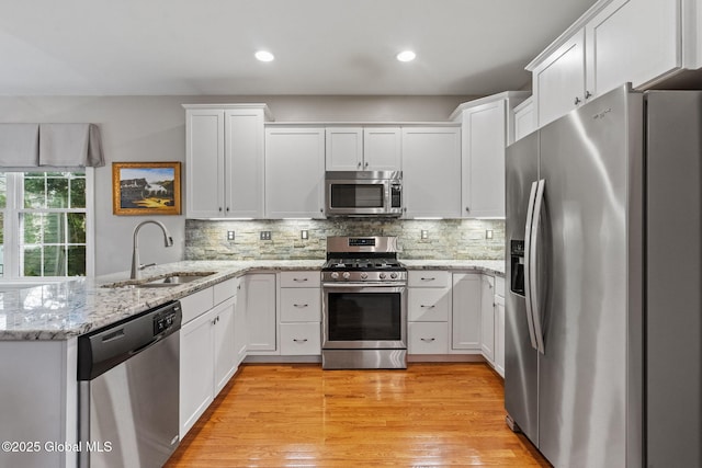 kitchen with stainless steel appliances, a sink, a peninsula, white cabinetry, and recessed lighting