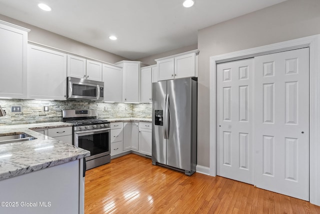 kitchen featuring appliances with stainless steel finishes, white cabinets, decorative backsplash, light wood finished floors, and recessed lighting