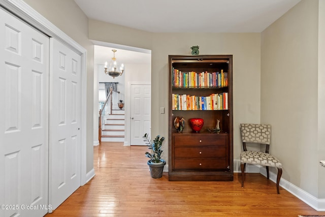 sitting room with light wood-style flooring, a chandelier, baseboards, and stairs