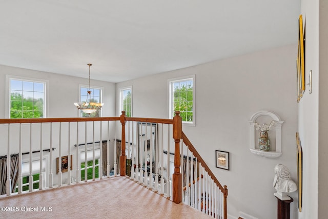 corridor with healthy amount of natural light, an upstairs landing, a chandelier, and baseboards