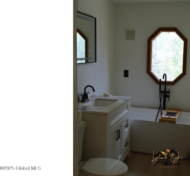 full bath with visible vents, a soaking tub, toilet, and vanity