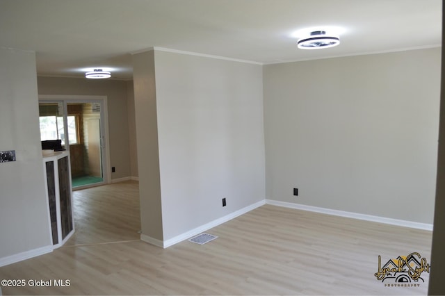 spare room featuring visible vents, light wood finished floors, crown molding, and baseboards