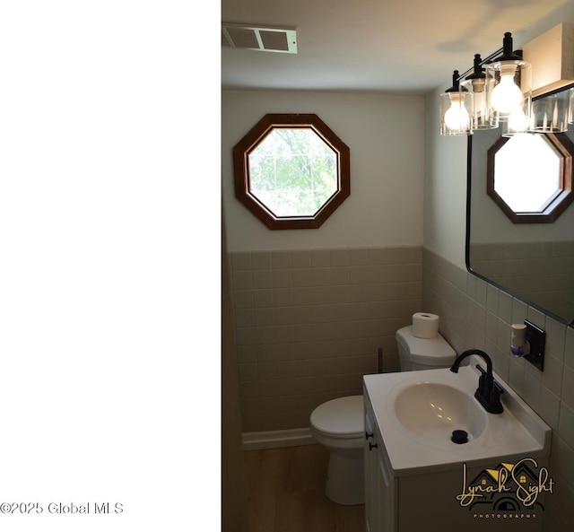 bathroom with visible vents, vanity, wood finished floors, toilet, and tile walls