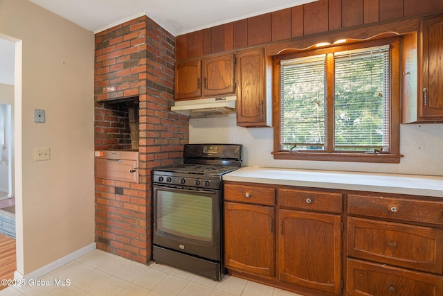 kitchen featuring black gas range oven, under cabinet range hood, light countertops, baseboards, and brown cabinets