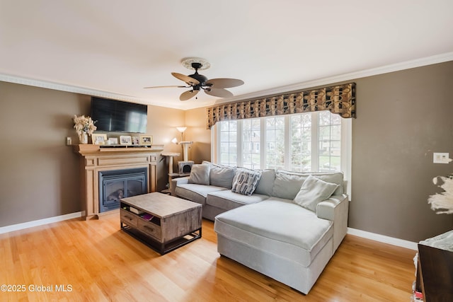 living area with crown molding, baseboards, a ceiling fan, and light wood-type flooring
