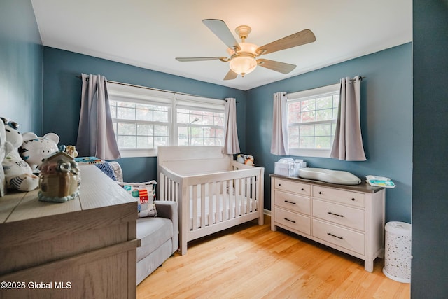 bedroom with light wood finished floors, a nursery area, and a ceiling fan