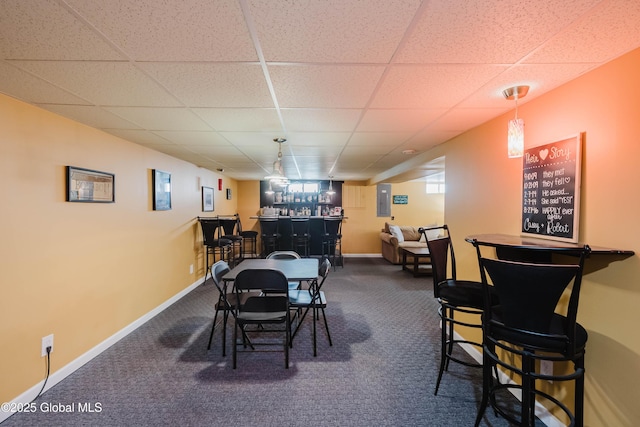 carpeted dining room featuring a bar, baseboards, and a drop ceiling