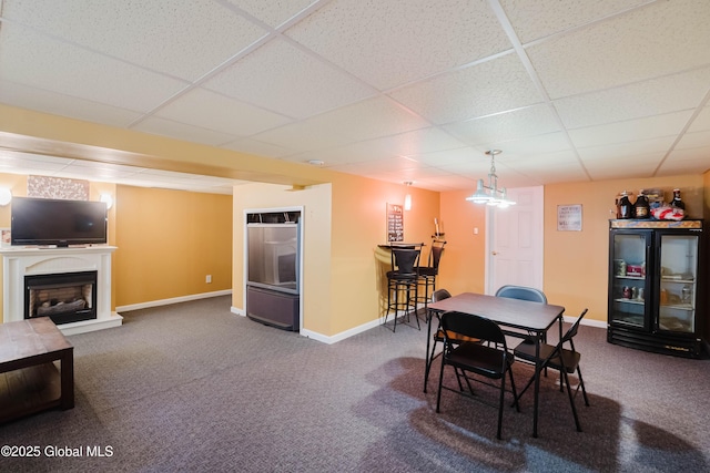 carpeted dining area featuring baseboards, a fireplace with raised hearth, and a drop ceiling