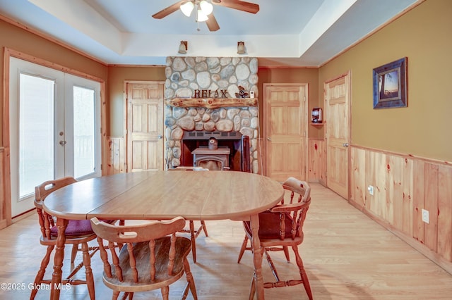 dining space with healthy amount of natural light, a ceiling fan, a tray ceiling, wainscoting, and wooden walls