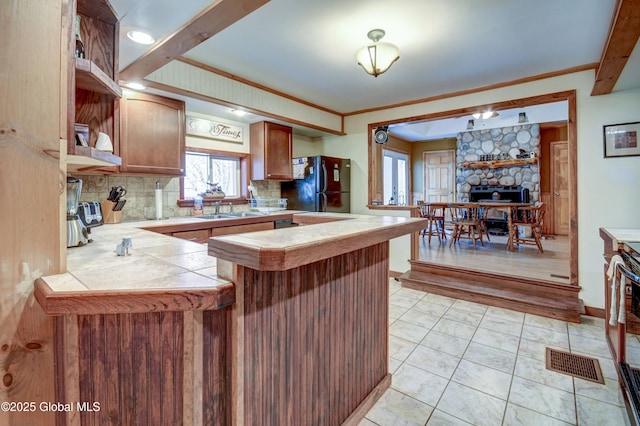 kitchen with freestanding refrigerator, a sink, a peninsula, decorative backsplash, and a stone fireplace