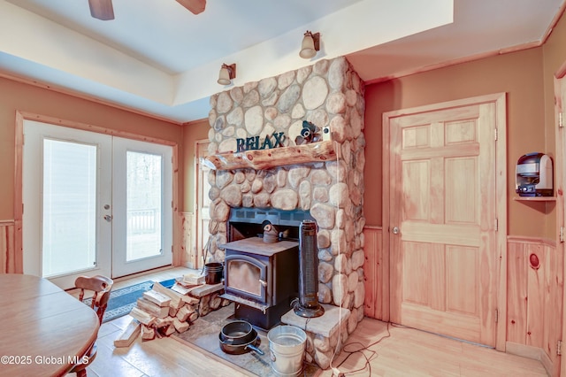 doorway with wainscoting, french doors, a wood stove, light wood finished floors, and a ceiling fan
