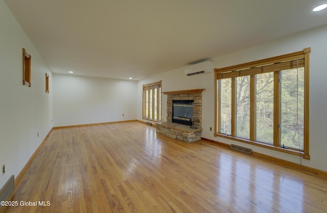 unfurnished living room featuring baseboards, a wall mounted air conditioner, a stone fireplace, recessed lighting, and hardwood / wood-style flooring