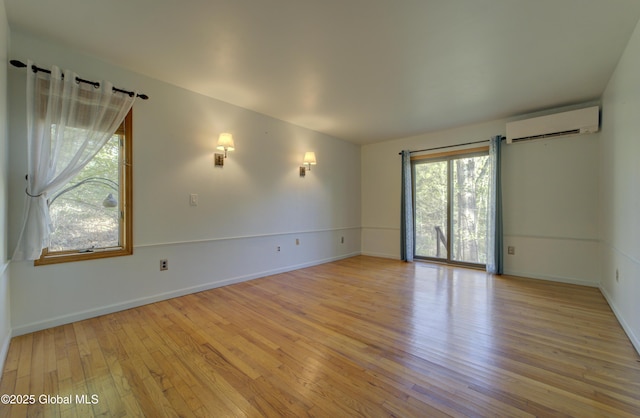 spare room featuring baseboards, a wall mounted AC, and light wood-style flooring