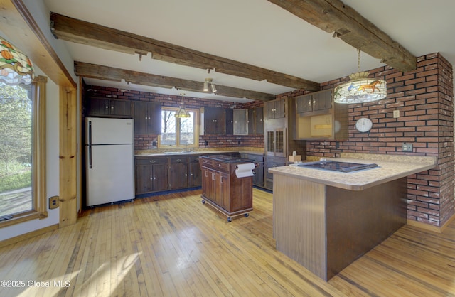 kitchen featuring dark brown cabinets, beamed ceiling, freestanding refrigerator, a peninsula, and light wood finished floors