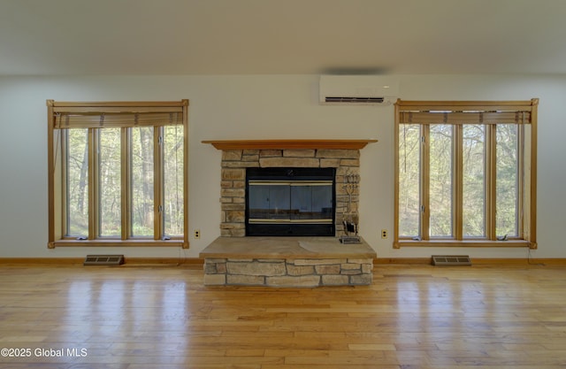 unfurnished living room with a stone fireplace, baseboards, a wall unit AC, wood finished floors, and visible vents