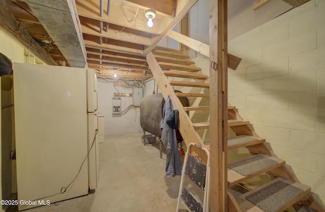 unfinished below grade area featuring freestanding refrigerator, stairway, heating fuel, electric panel, and concrete block wall
