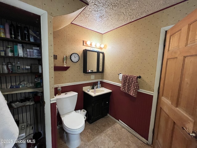half bath featuring vanity, wallpapered walls, wainscoting, and toilet