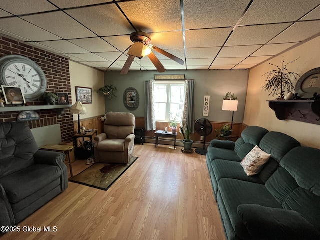 living area with wood finished floors, a ceiling fan, a paneled ceiling, and a wainscoted wall