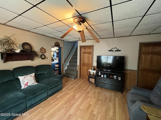 living room featuring stairs, ceiling fan, a drop ceiling, and wood finished floors