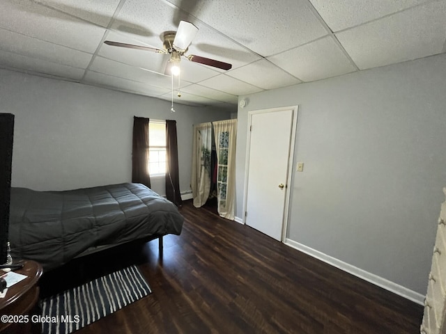 bedroom featuring baseboard heating, a ceiling fan, wood finished floors, and a paneled ceiling