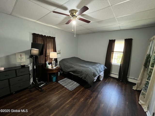 bedroom featuring ceiling fan, a baseboard heating unit, a paneled ceiling, and wood finished floors