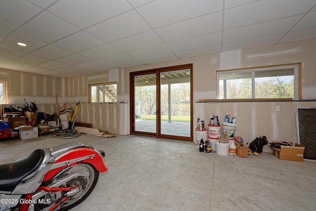 living room featuring unfinished concrete floors, a paneled ceiling, and a wealth of natural light