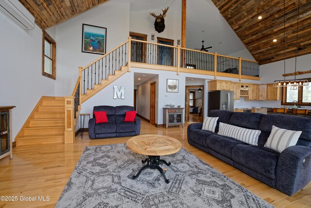 living area with an AC wall unit, light wood-style flooring, high vaulted ceiling, and stairway
