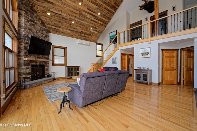 living area with a stone fireplace, high vaulted ceiling, an AC wall unit, stairs, and hardwood / wood-style floors
