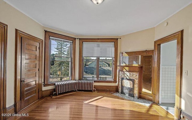 unfurnished living room with wood finished floors, a fireplace with flush hearth, baseboards, and radiator heating unit
