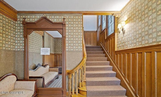 stairs featuring a decorative wall, ornamental molding, wainscoting, and wallpapered walls
