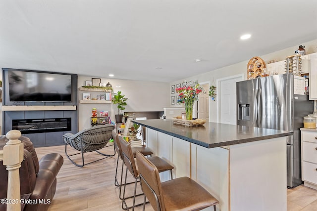 kitchen with a kitchen island, white cabinetry, a glass covered fireplace, stainless steel fridge, and light wood-style flooring