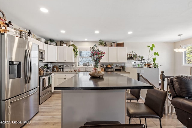kitchen with white cabinetry, a kitchen bar, dark countertops, and stainless steel appliances
