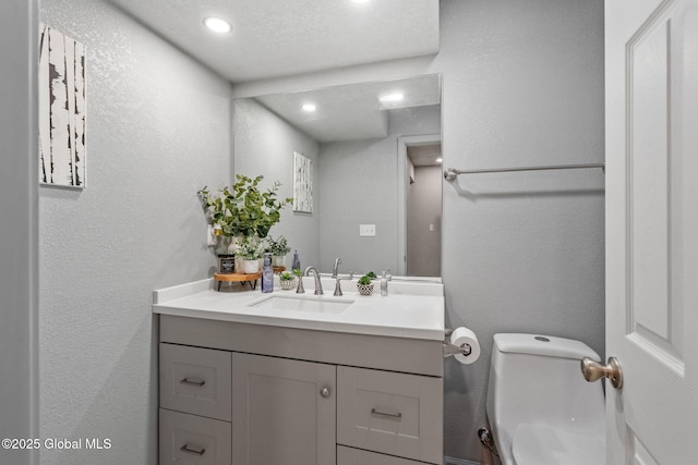 bathroom featuring recessed lighting, vanity, a textured wall, and toilet